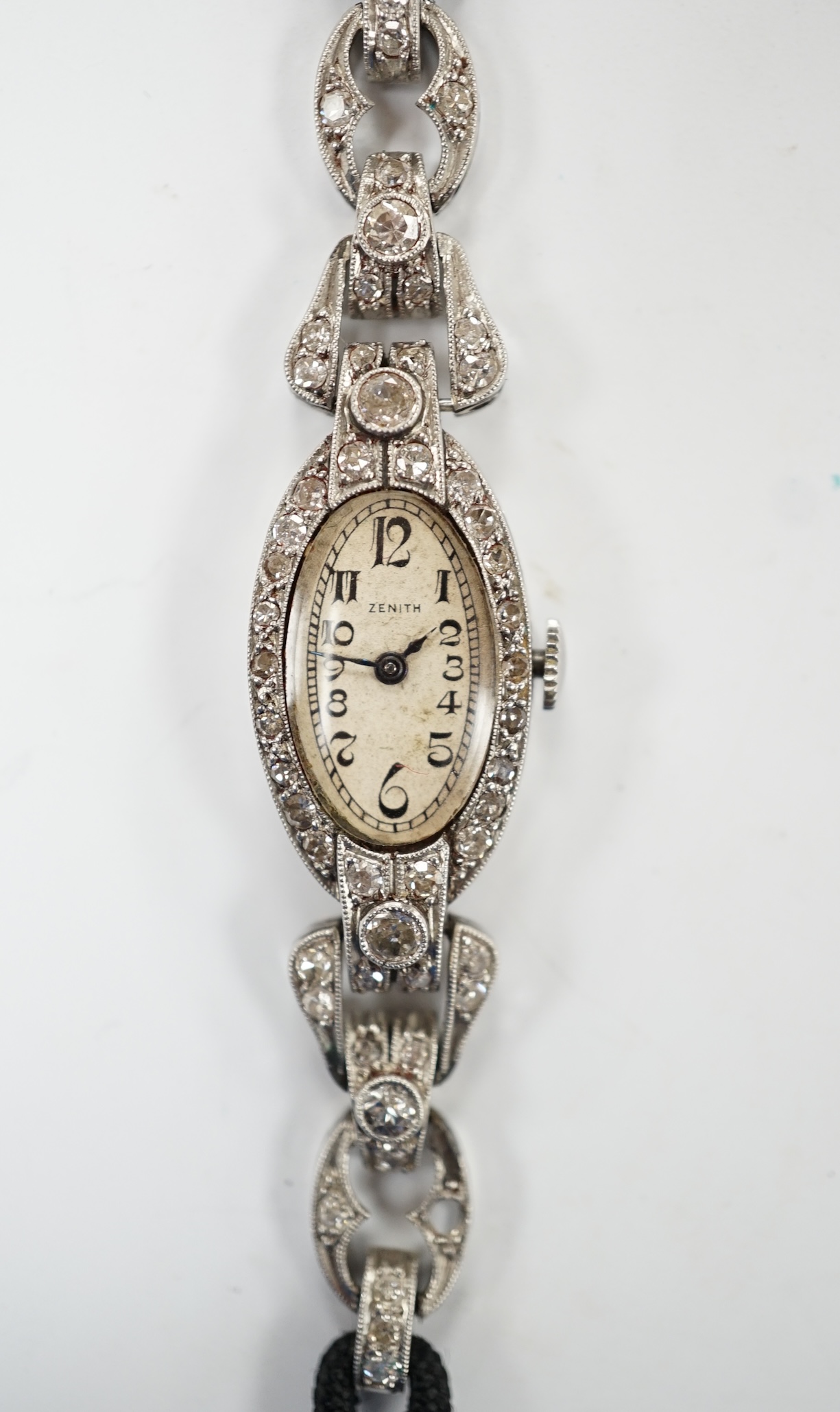 A lady's Zenith white metal and diamond cluster set manual wind oval cocktail watch, on a twin fabric strap, 15cm, gross weight 16.7 grams. Fair condition.
